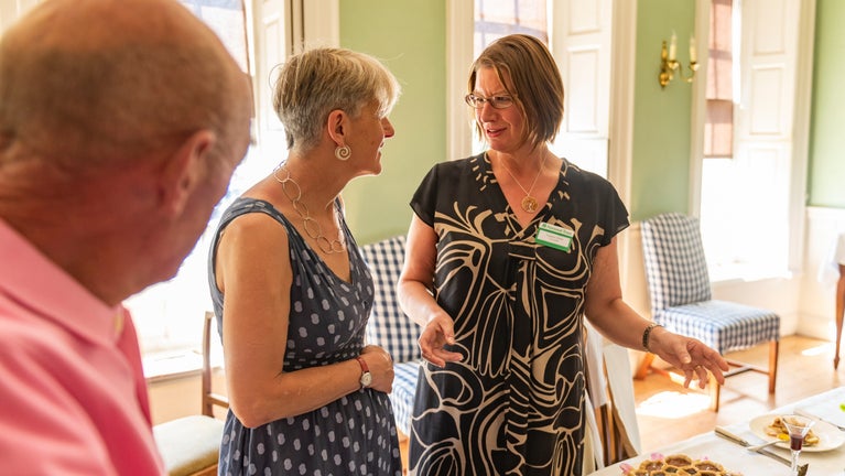 Two guests listen to a volunteer talking about the history of Wordsworth House and Garden in the dining room while standing over a table with traditional Georgian dishes